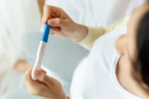 happy pregnant woman holding pregnancy test examine positive te - Медицински център "Орто Пункт"
